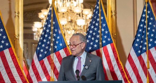 Senator Chuck Schumer stands at a podium with American Flags behind him